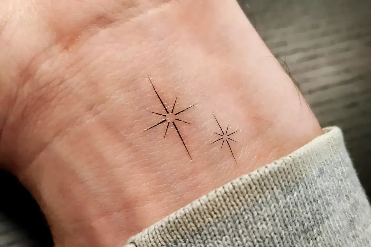 Delikatny tatuaż gwiazda na nadgarstku, dwie małe, błyszczące gwiazdki symbolizujące marzenia.