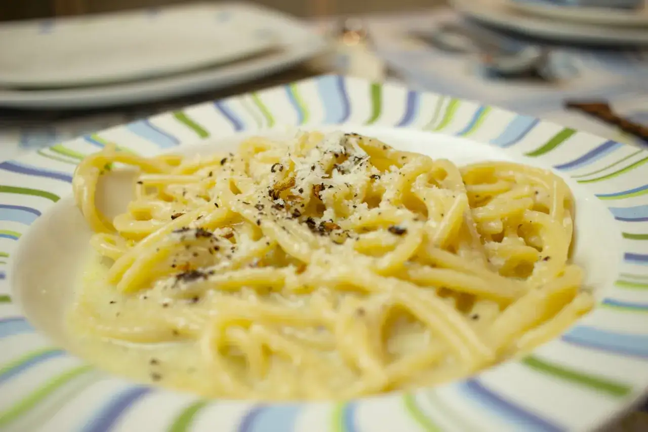 Un plat de tonnarelli cacio e pepe, des pâtes crémeuses saupoudrées de fromage râpé et de poivre noir, sur une assiette rayée.