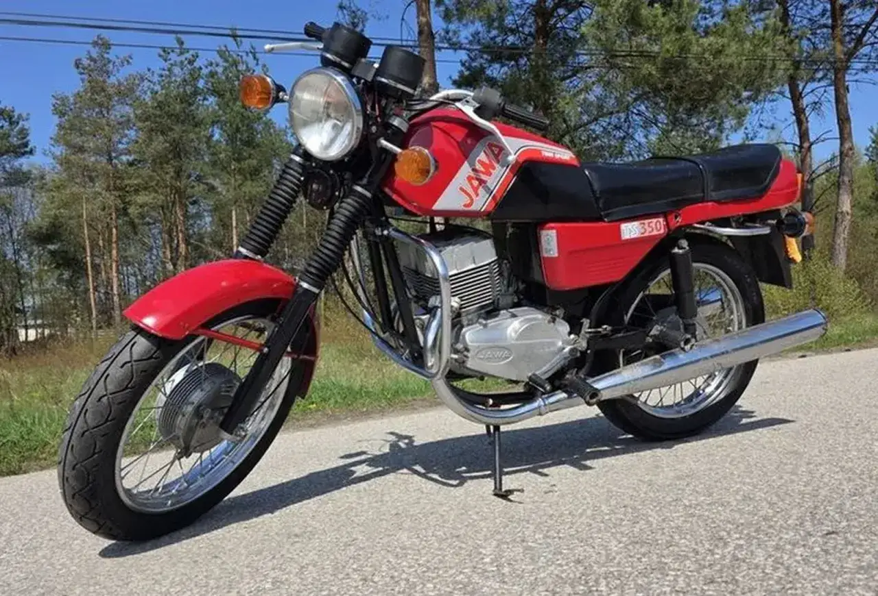 Czerwony motocykl Jawa TS 350, jeden z klasycznych modele wsk, zaparkowany na drodze leśnej.