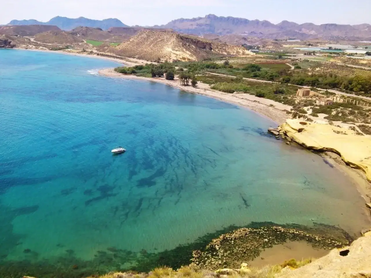 Aguas turquesas y arena dorada en la **playa Pulpi**, con una pequeña embarcación navegando y montañas áridas al fondo.