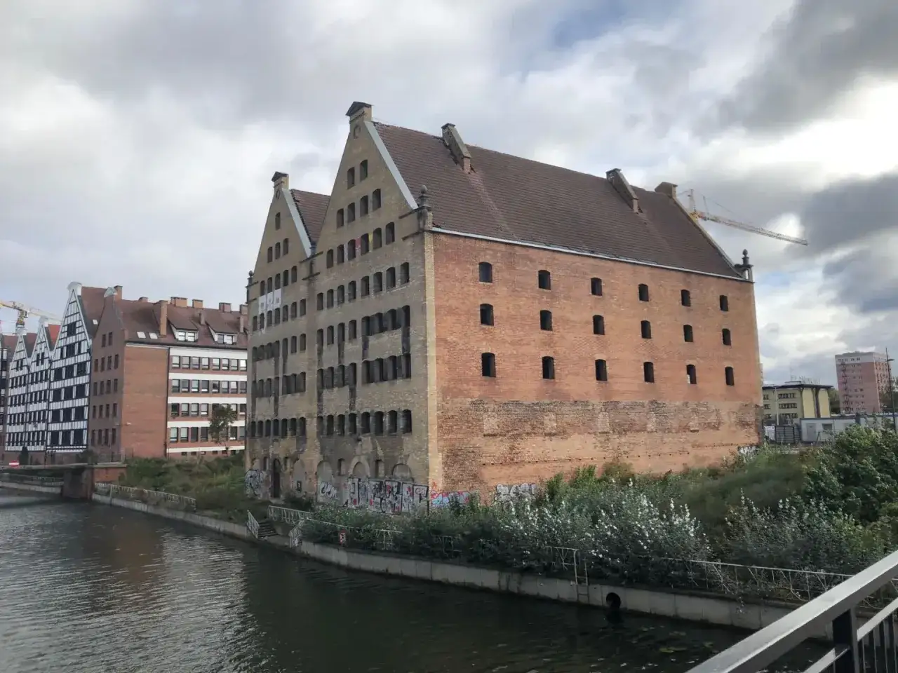 Historyczny spichlerz w Gdańsku nad Motławą, z charakterystyczną ceglaną fasadą i licznymi oknami.