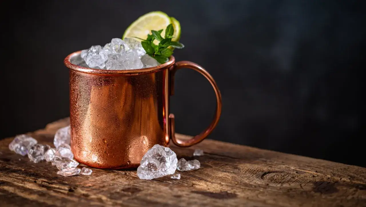 Miedziany kubek z lodem, limonką i miętą, idealny na orzeźwiającego Moscow Mule.