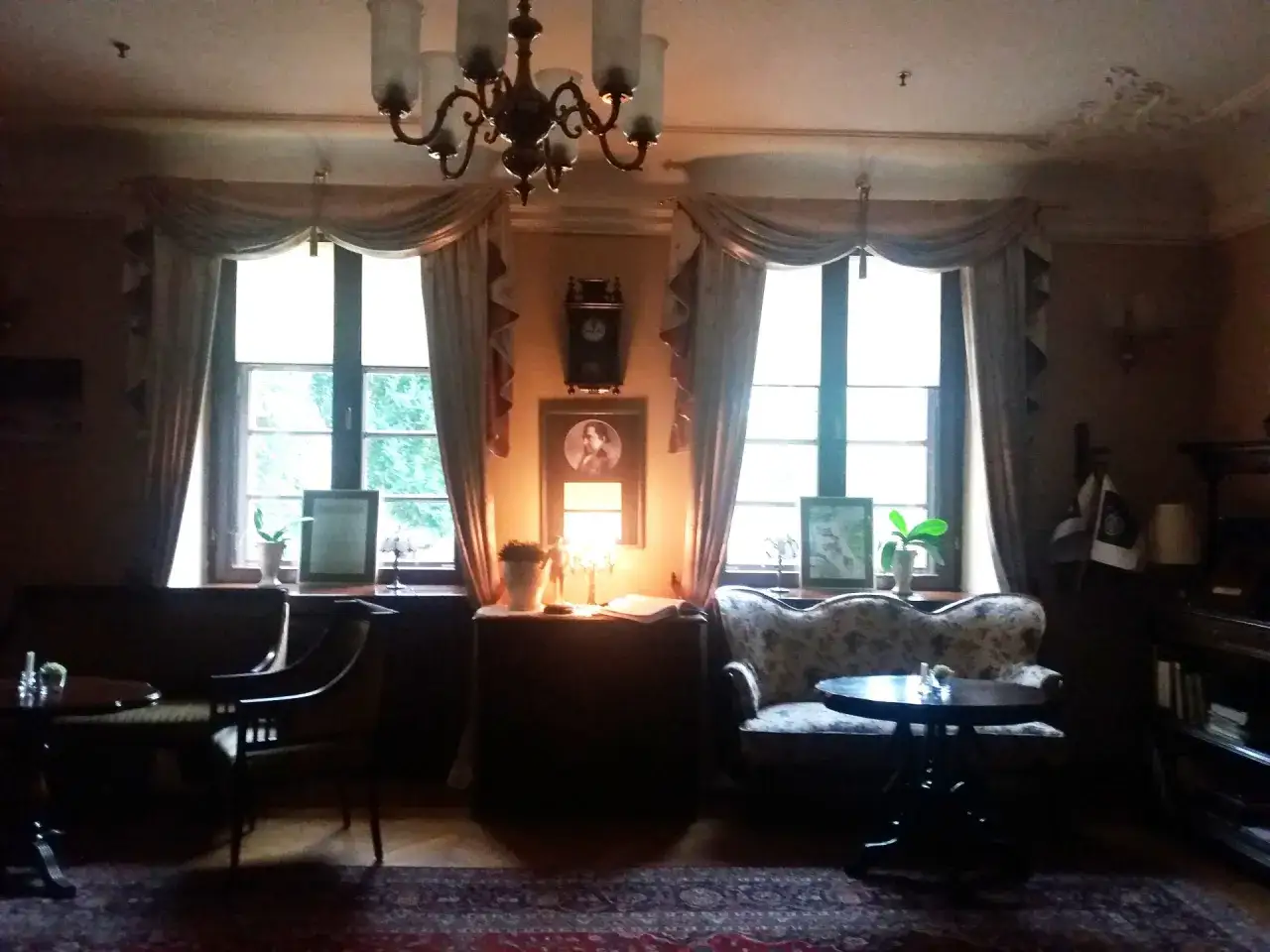 Wnętrze pałacu w Krokowej: elegancka sofa, stolik, obrazy i zabytkowy zegar przy oknie.