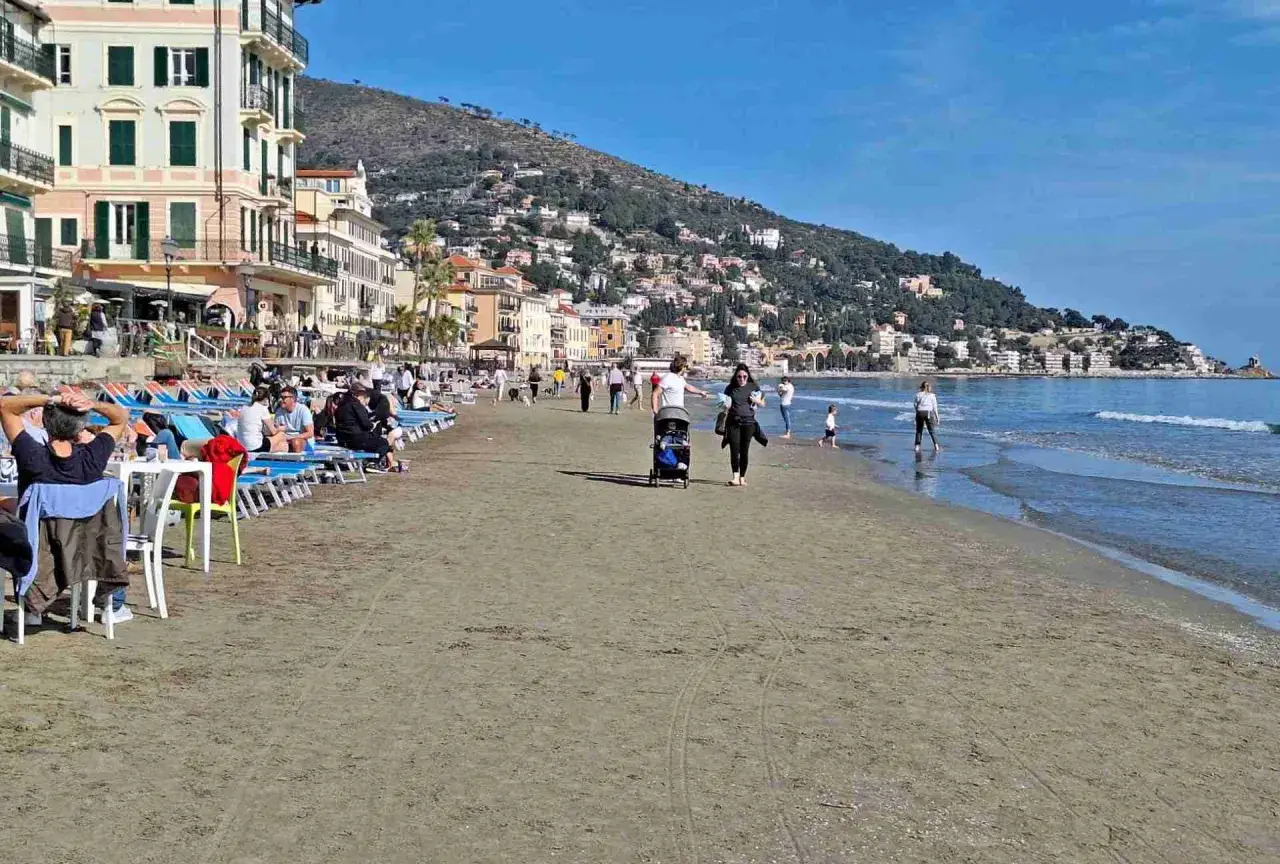 Plage anim&eacute;e &agrave; San Bartolomeo al Mare, avec des gens se relaxant sur des chaises longues et se promenant pr&egrave;s de la mer, sous un ciel bleu.
