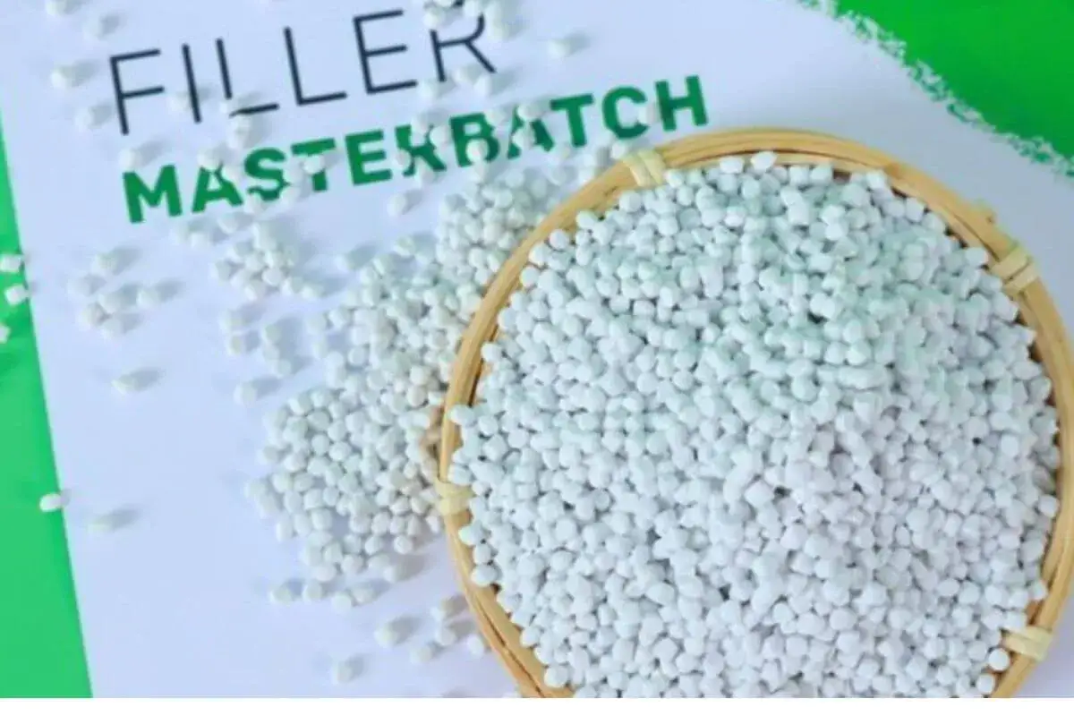 Białe granulki plastiku, prawdopodobnie masterbatch, rozsypane na papierze z napisem