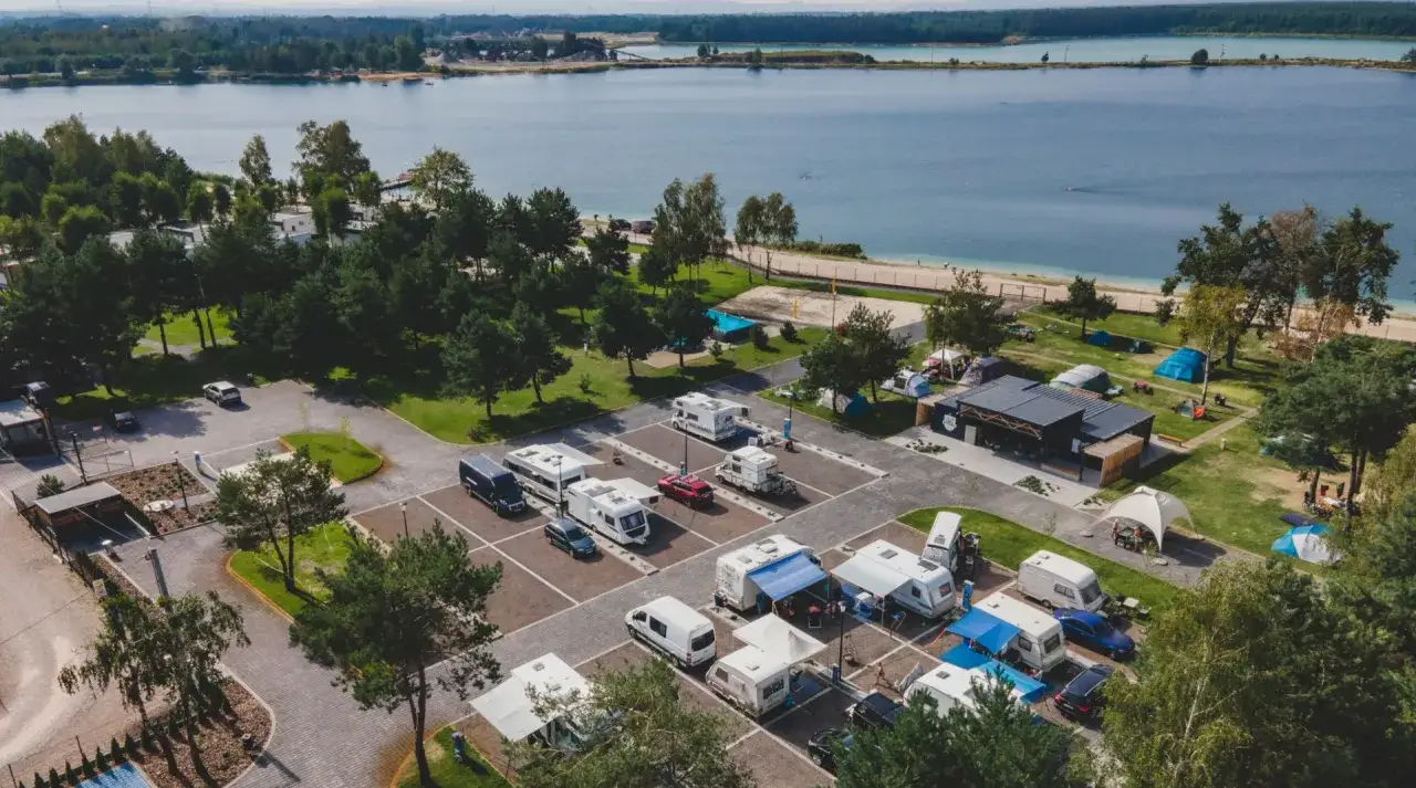Widok z lotu ptaka na **riviera camp** z kamperami, namiotami i budynkiem restauracyjnym nad jeziorem.