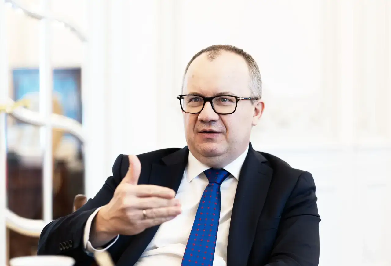 Wiceminister sprawiedliwości w okularach, w garniturze i niebieskim krawacie z czerwonymi wzorami, gestykuluje prawą ręką.