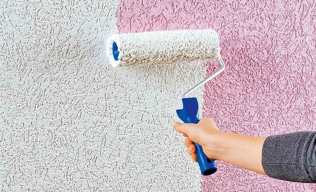 Eine Hand rollt mit einem Strukturroller **streichputz innen** auf eine wei&szlig;e Wand, die sich zur rechten Seite in Rosa wandelt.