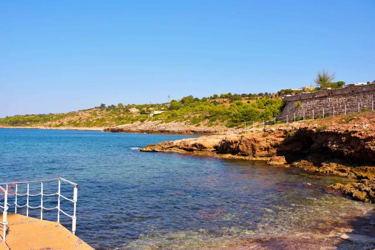 Scogliera rocciosa e mare cristallino a San Gregorio Salento, con una piccola piattaforma in primo piano.