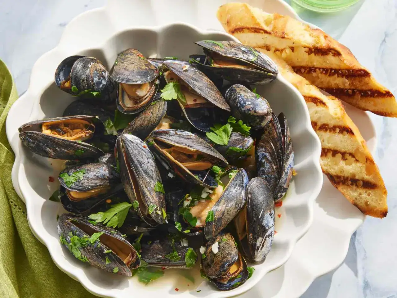 Un plato generoso de mejillones al vapor, adornados con perejil fresco y servidos con pan tostado a la parrilla.