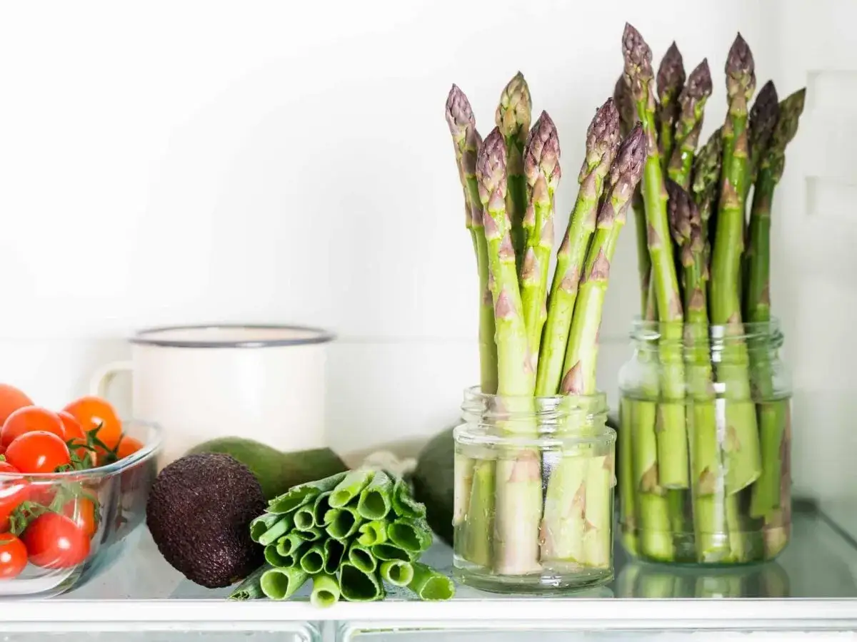 Asparagi freschi in barattoli con acqua: un ottimo modo per conservare gli asparagi e mantenerli croccanti. Vicino, pomodorini, avocado e cipollotti.