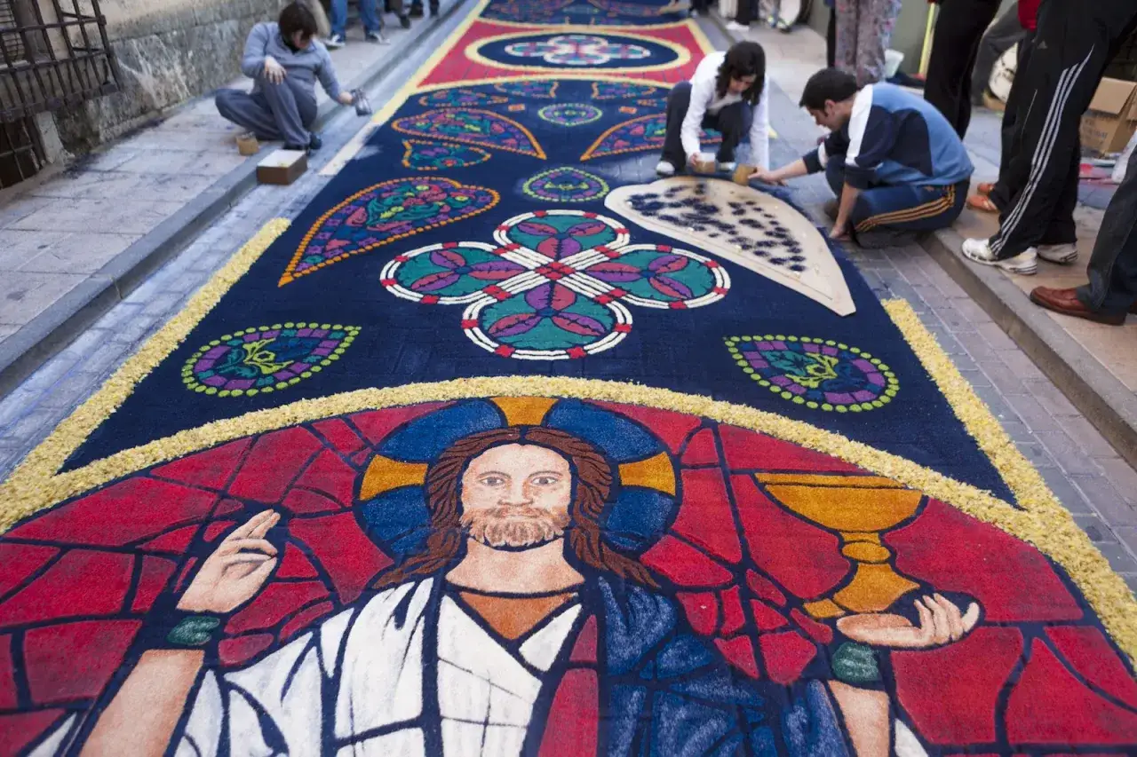 Alfombras de serrín en Elche de la Sierra, con una imagen de Jesucristo y motivos florales, creadas por artesanos.