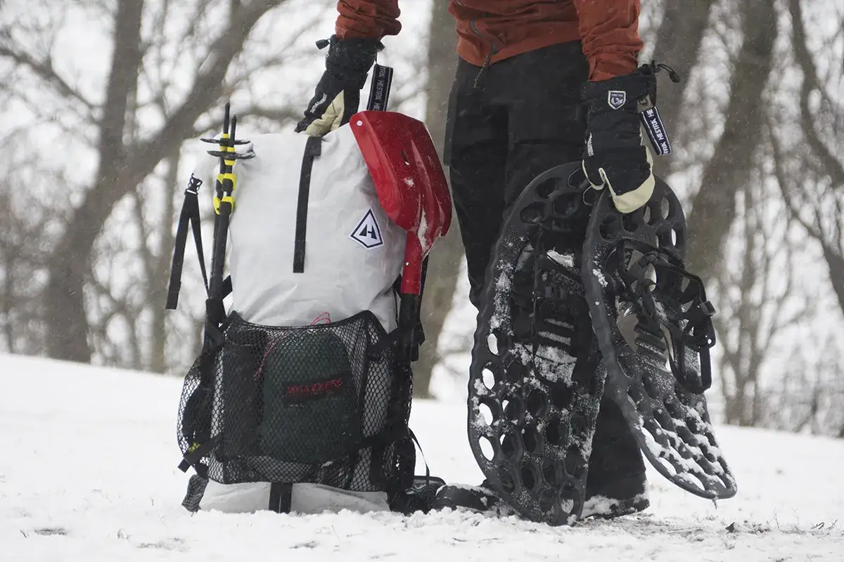 Person med ryggs&auml;ck, sn&ouml;skor och spade redo f&ouml;r en resa p&aring; vintern i sn&ouml;ig skog.