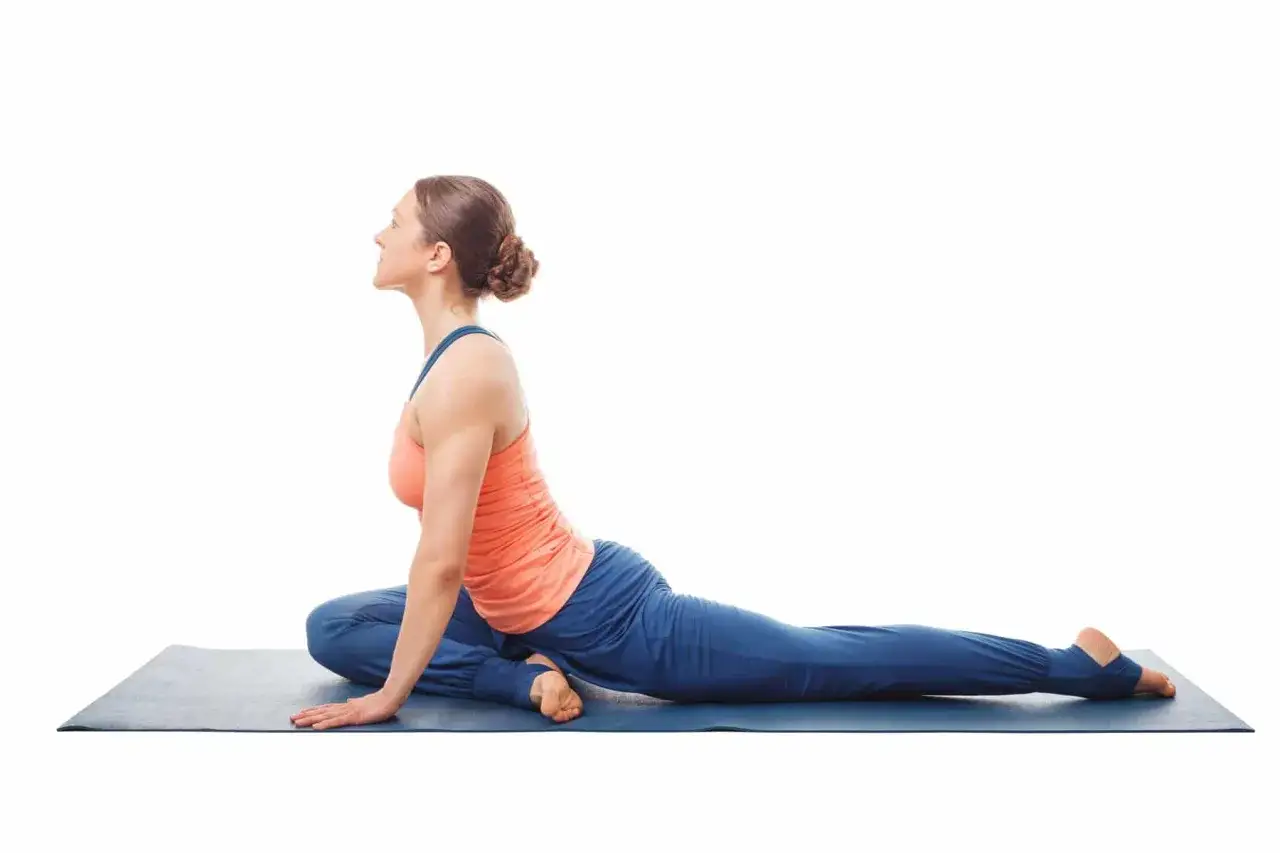 Femme en posture du pigeon sciatique sur un tapis de yoga bleu, le corps pench&eacute; en avant, une jambe pli&eacute;e sous elle, l'autre &eacute;tendue derri&egrave;re.