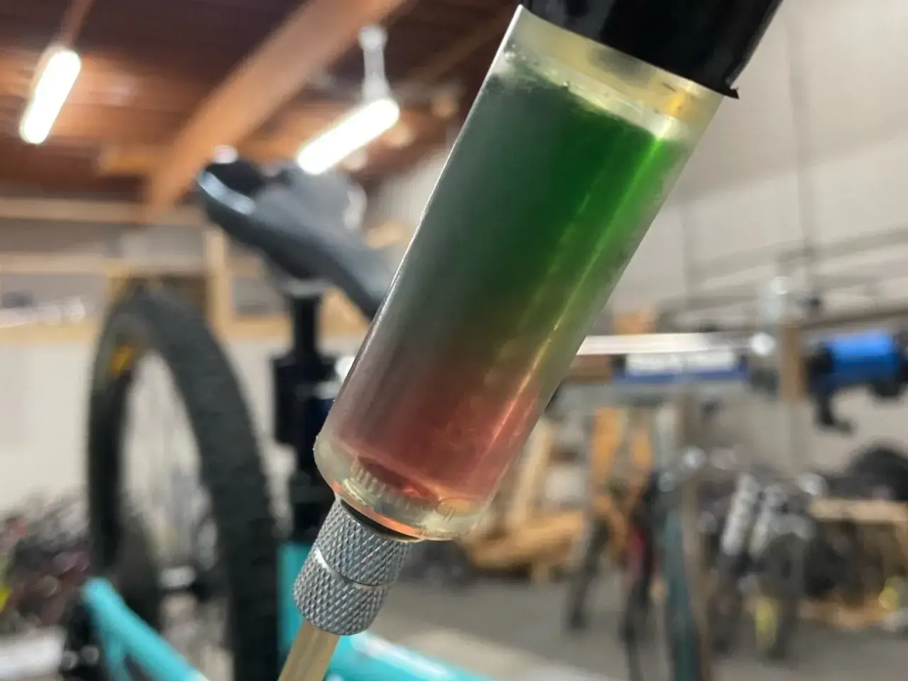A syringe filled with red and green synthetic brake fluid, indicating a potential compatibility issue during a bike maintenance task.