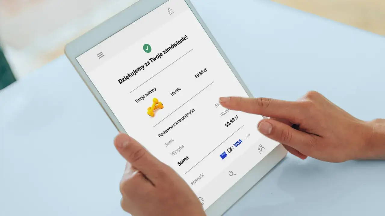 Dłonie na tablecie pokazują podsumowanie zamówienia. Widać ikonę Visa, co sugeruje, jak płacić kartą Visa przez internet.