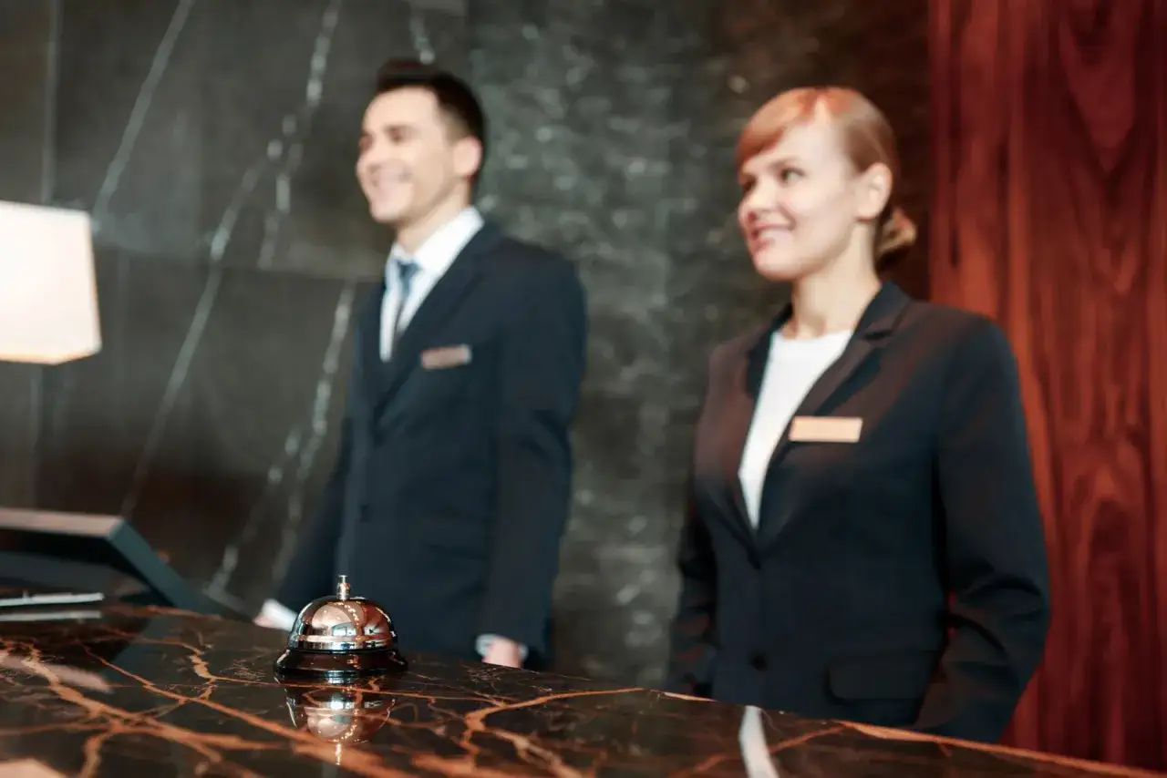 Uśmiechnięci pracownicy hotelowi w eleganckim dress code, gotowi do obsługi gości przy recepcji.