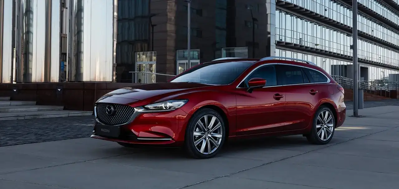 Czerwona Mazda 6 2.0 benzyna kombi zaparkowana przed nowoczesnym budynkiem.