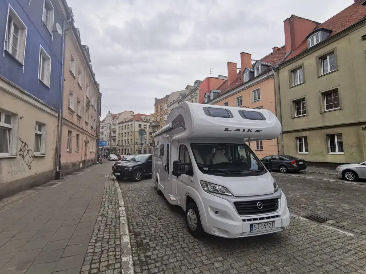 Biała kampera zaparkowana na brukowanej ulicy w Poznaniu zimą. W tle kamienice i inne samochody.