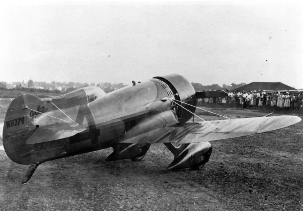 Ein altes Flugzeug, eine **Gee Bee** Rennmaschine, steht auf einem Feld. Eine Menschenmenge beobachtet das historische Fluggerät.