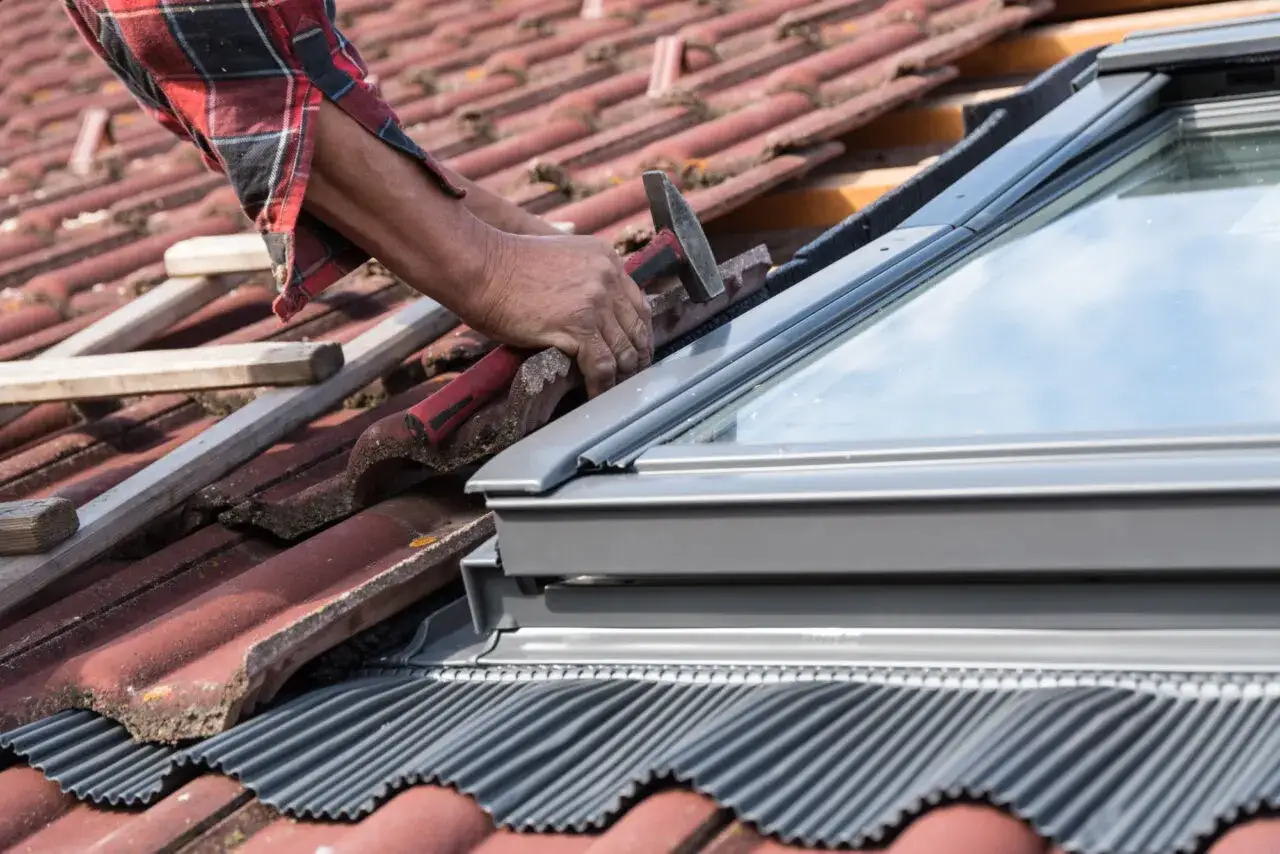 Hand repariert Dachkehle mit Hammer und Ziegeln, um das Dachfenster abzudichten.