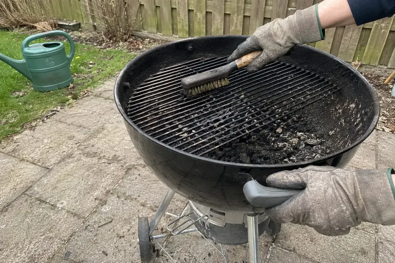 Mit Handschuhen wird der Grillrost gereinigt. Asche und Ru&szlig; werden mit einer B&uuml;rste entfernt, damit das n&auml;chste Grillvergn&uuml;gen beginnen kann.