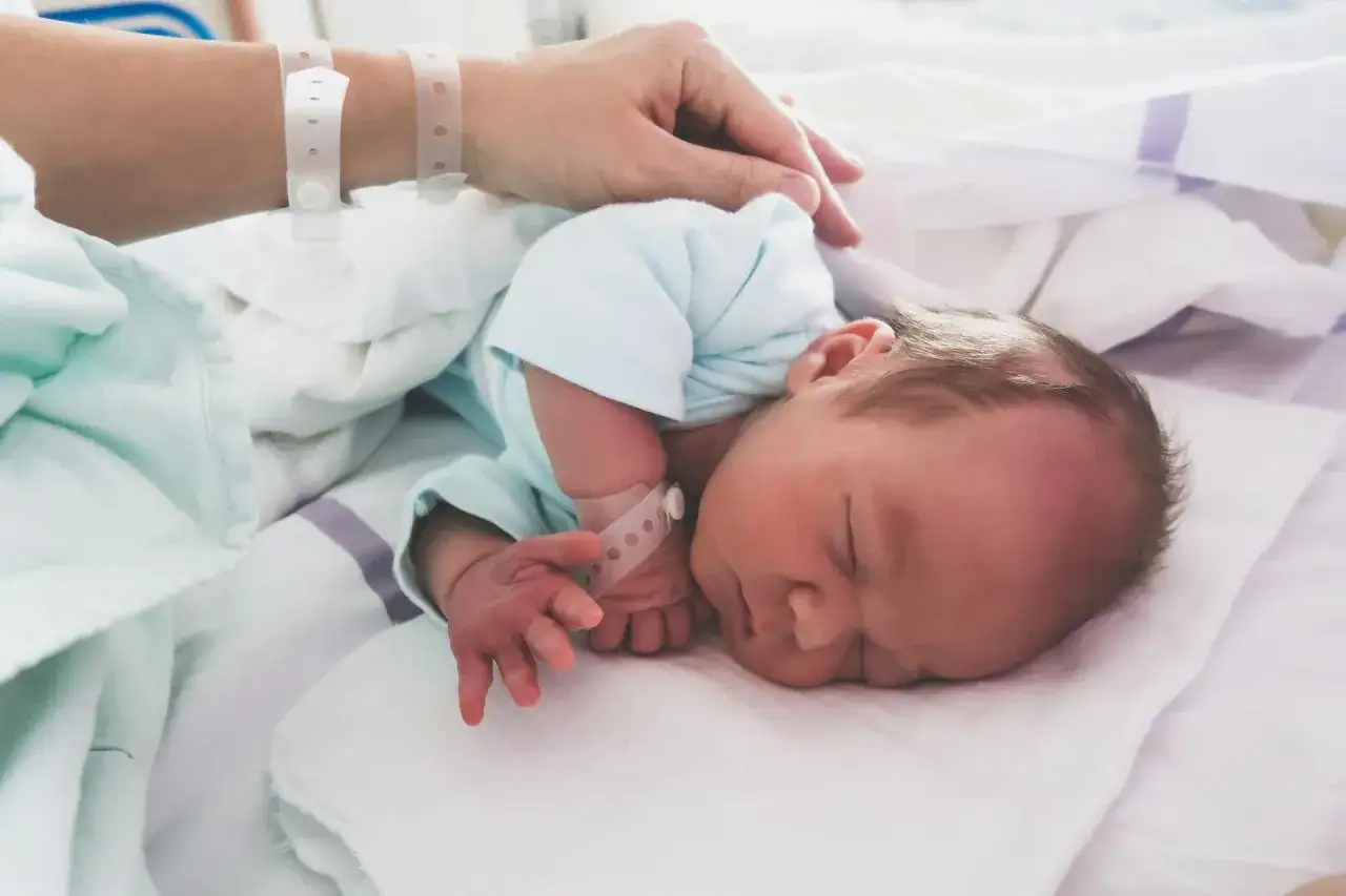 Noworodek śpi w szpitalnym łóżeczku, otoczony troską. Mama głaszcze go po główce. Dziecko ma opaskę identyfikacyjną, która może być ważna w przypadku podejrzenia cytomegalii.