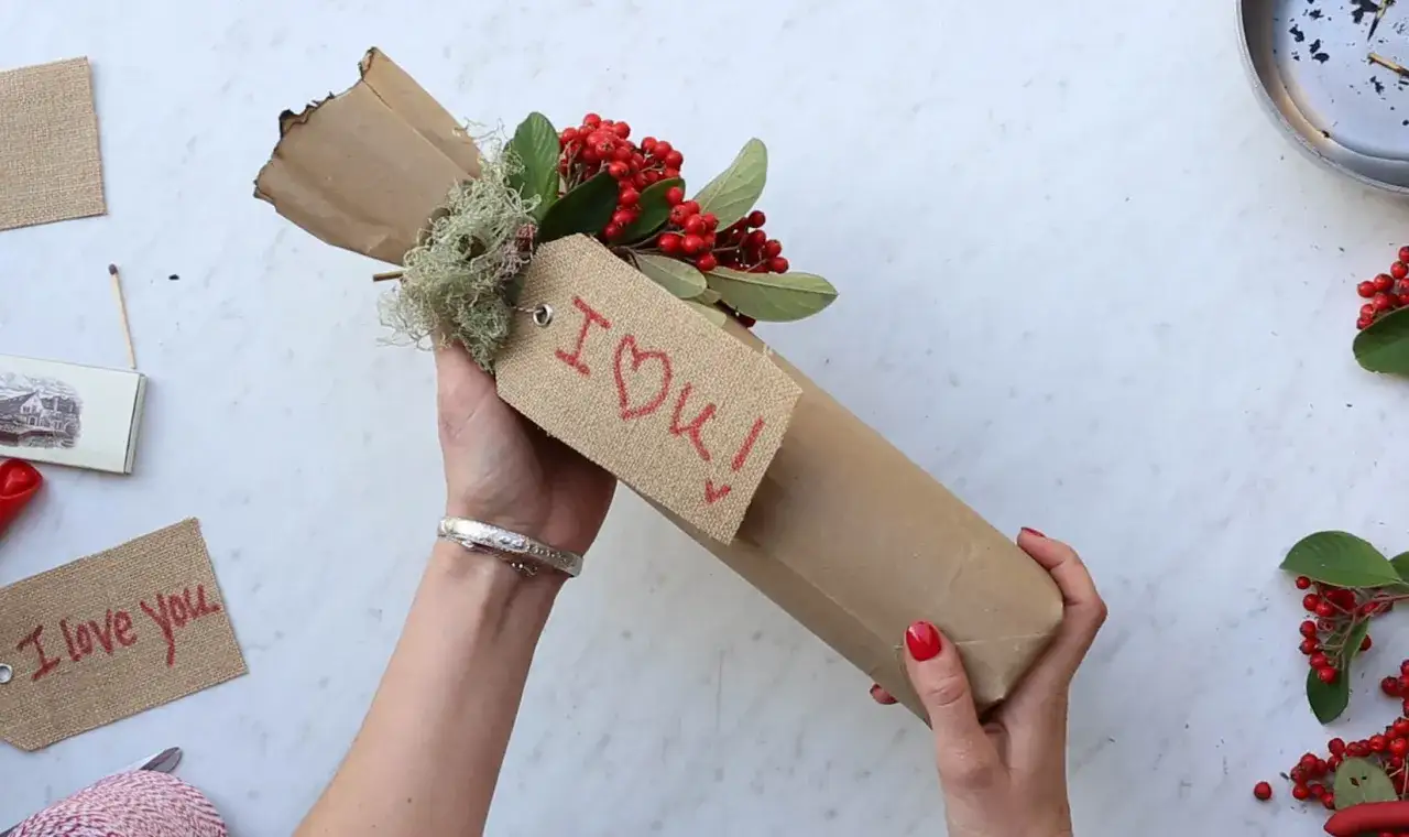 Eine Weinflasche verpacken mit braunem Papier, Moos, Beeren und einem Anhänger mit der Aufschrift