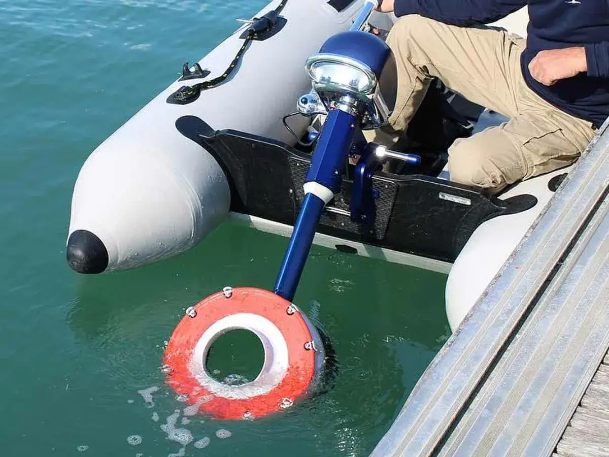 Bateau gonflable avec un moteur électrique bleu et rouge, pas d'une hélice visible, dans l'eau claire.