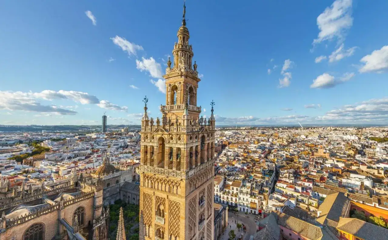 La Giralda, torre emblemática de la catedral sevilha, se alza majestuosa sobre la ciudad bajo un cielo azul con nubes.