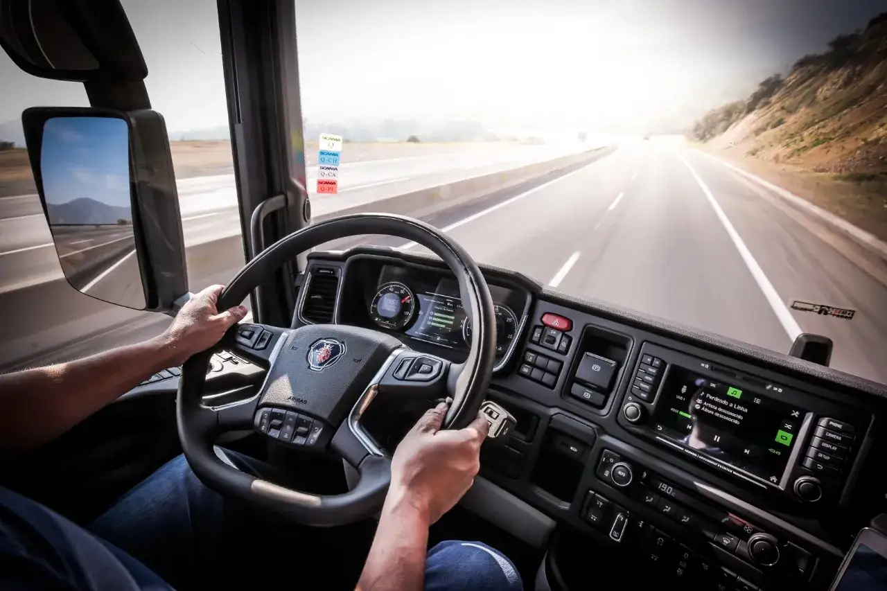 Ręce kierowcy na kierownicy Scania R, jadącej autostradą. Widok z kabiny ciężarówki.