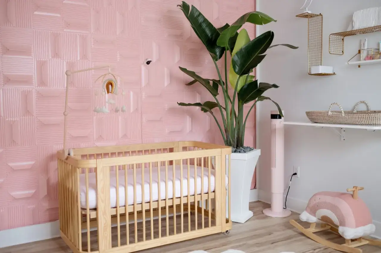 Lit en bois, mobile arc-en-ciel, plante verte et mur texturé rose pour une **diy déco chambre bébé** douce et tendance.