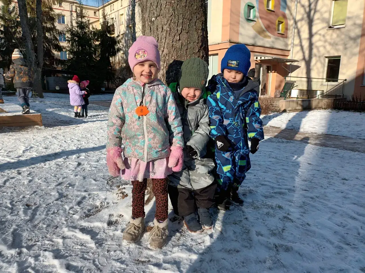 Trójka dzieci w zimowych ubraniach, gotowa na hartowanie dzieci w Norwegii. Śnieg wokół, słońce i uśmiechy.