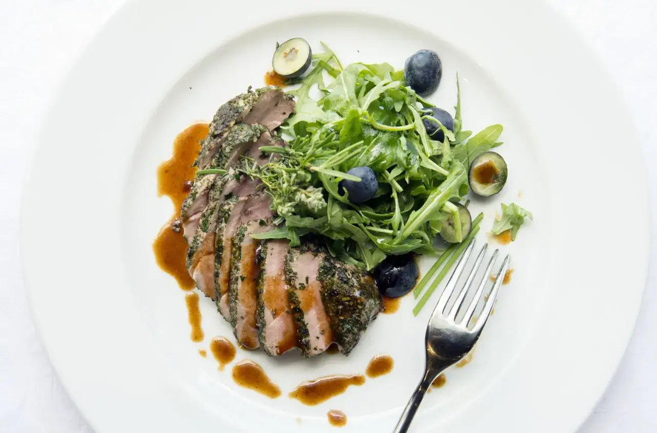 Fetta di filetto di maiale alle erbe, servita con insalata di rucola, mirtilli e salsa bruna.