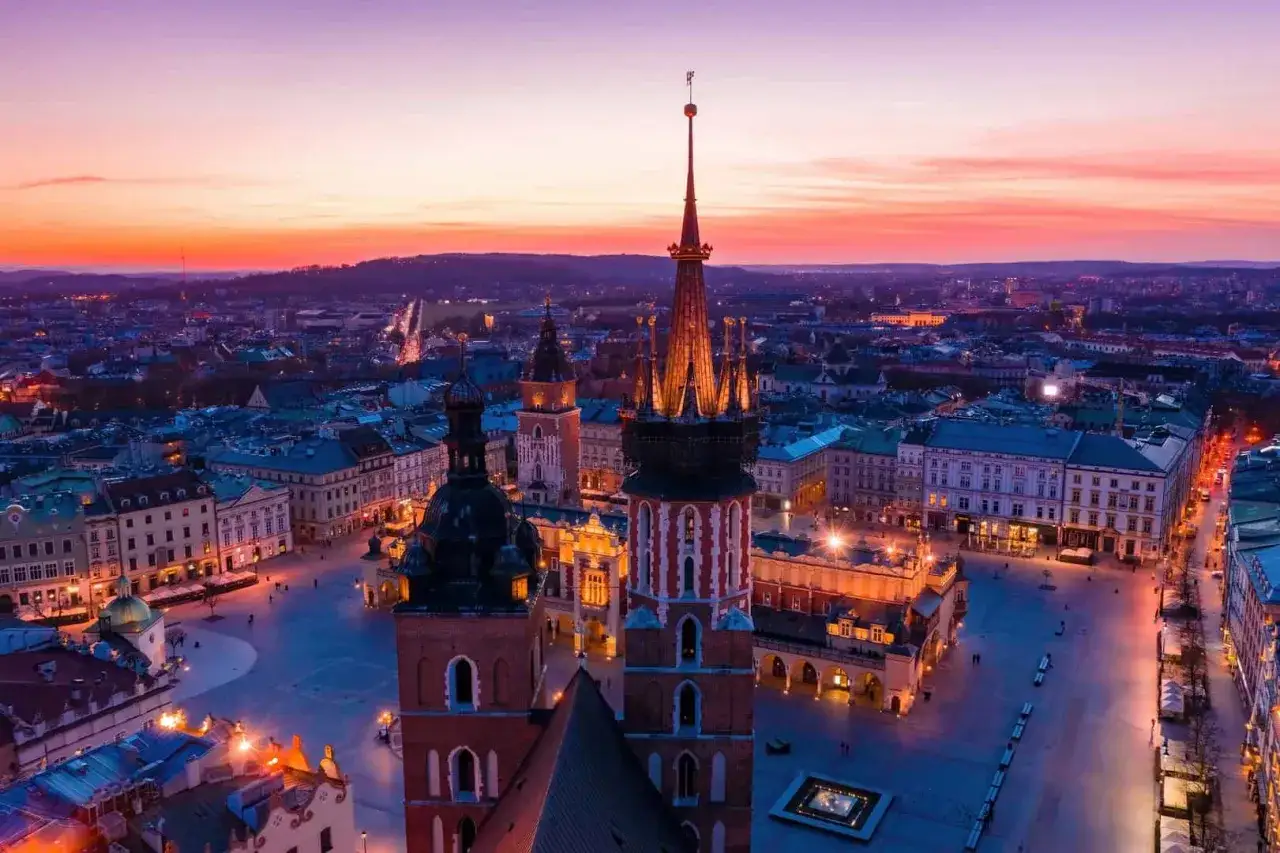 Zach&oacute;d słońca nad Rynkiem Gł&oacute;wnym w Krakowie, gdzie widać najcenniejsze zabytki krakowa: Sukiennice i Kości&oacute;ł Mariacki.