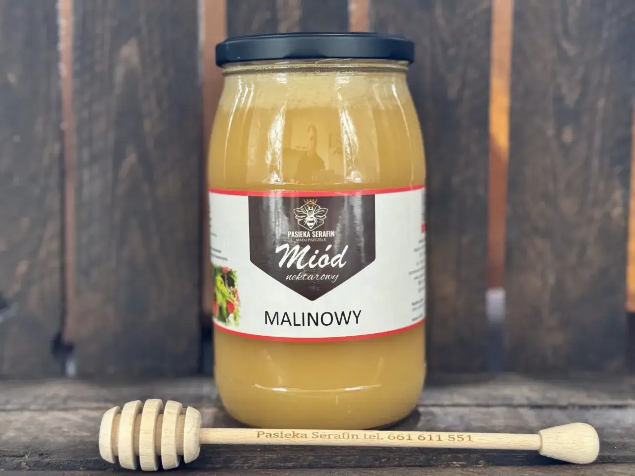 Słoik miodu malinowego z pasieki Serafin. Obok drewniana łyżka do miodu.