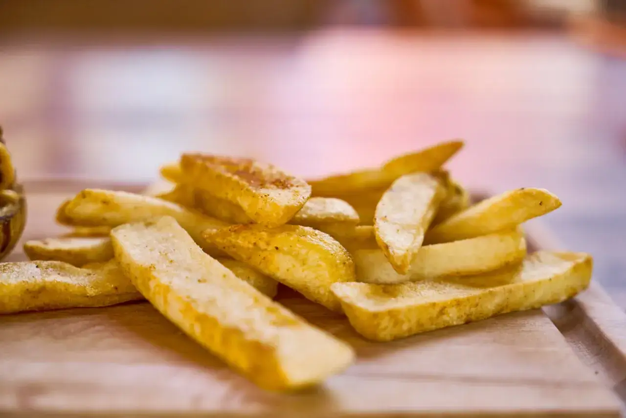 Złociste, chrupiące frytki z McDonald's, ułożone na drewnianej desce, kuszą swoim wyglądem.
