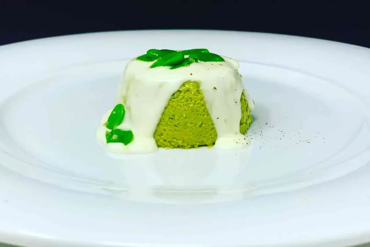 Sformato di pecorino verde brillante, nappato con una salsa bianca e guarnito con foglie verdi.