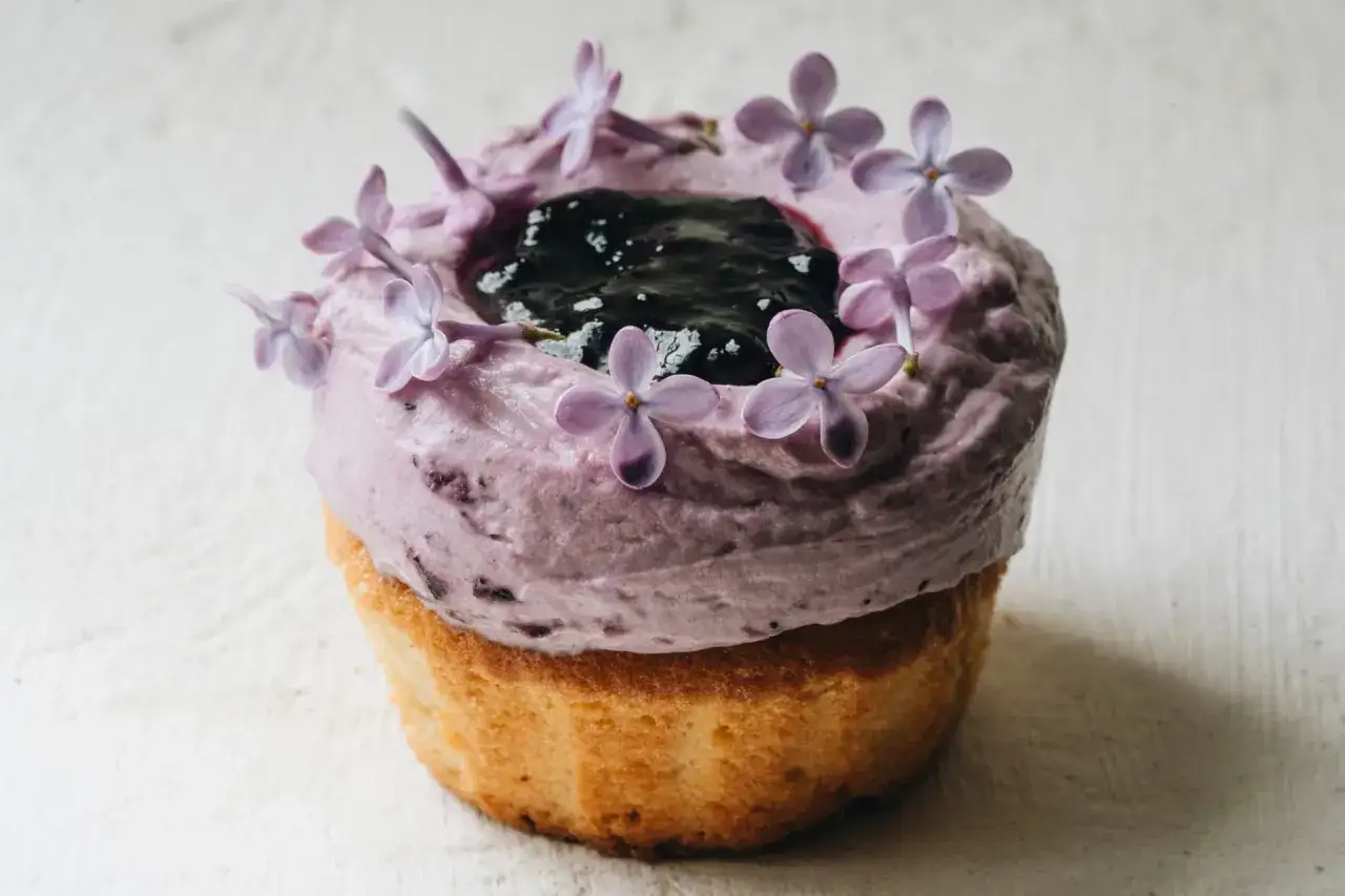 En lila frosting med blåbär och syrenblommor toppar en gyllene cupcake. Ett perfekt recept för cupcakes!