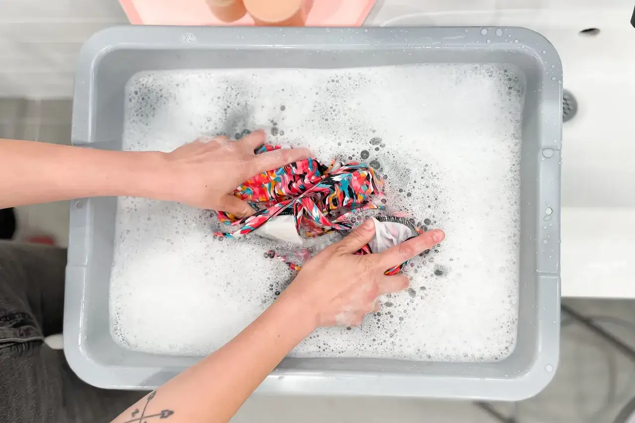 H&auml;nde waschen ein buntes bikini in schaumigem Wasser.