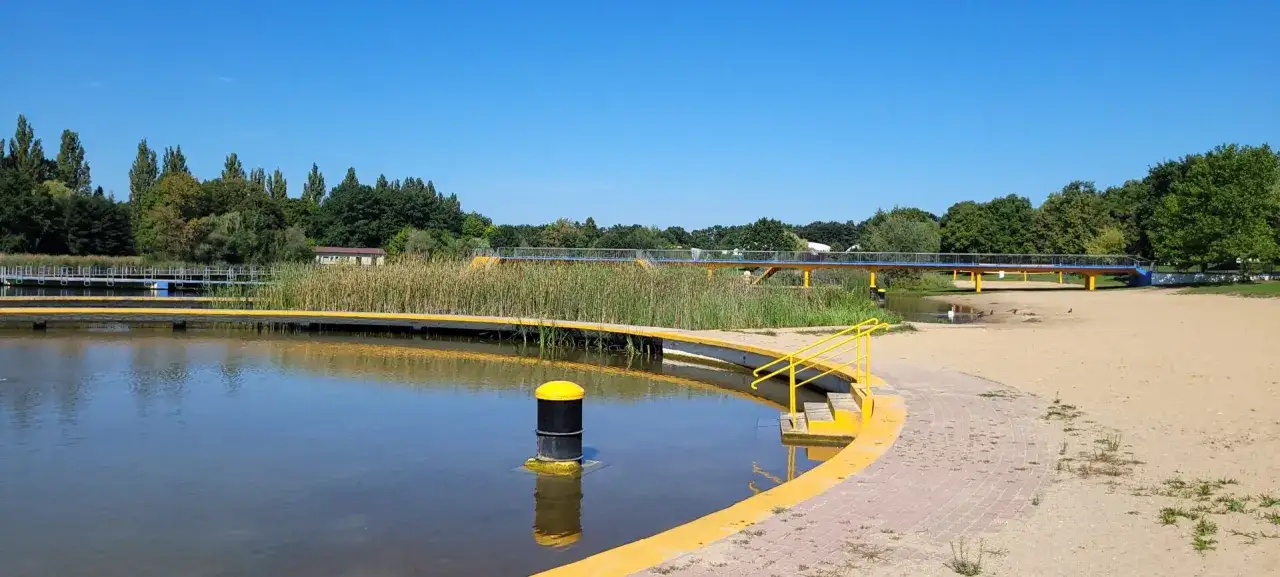 Morskie Oko Wrocław: piaszczysta plaża, łagodne zejście do wody, żółte balustrady i mostek nad trzcinami.