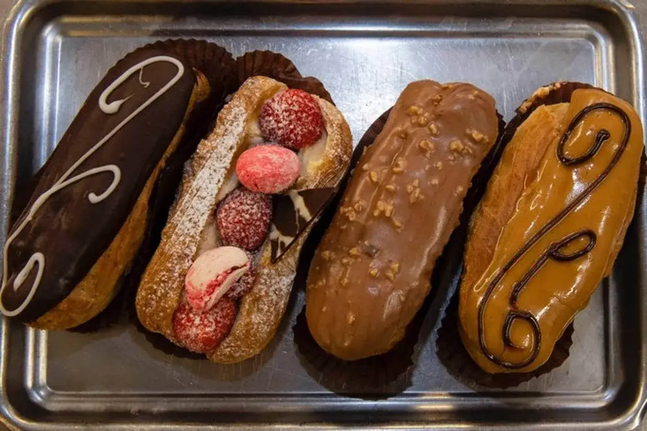 Quatre &eacute;clairs vari&eacute;s sur un plateau : un au chocolat noir, un garni de fruits rouges et macarons, un au chocolat pralin&eacute;, et un &agrave; la cr&egrave;me caramel.