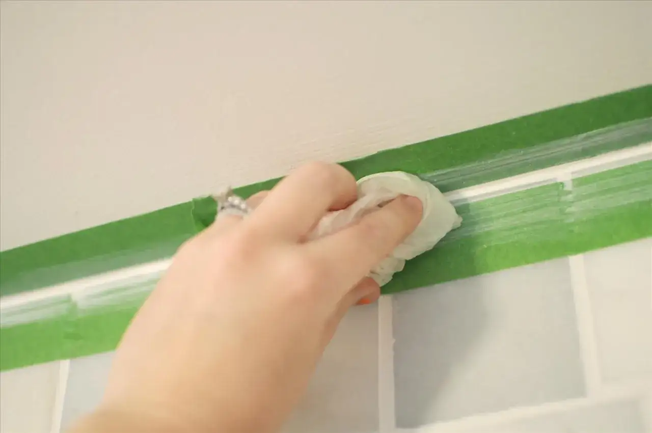 A hand with a ring smooths caulk along a taped seam. This shows how to caulk for a clean finish.
