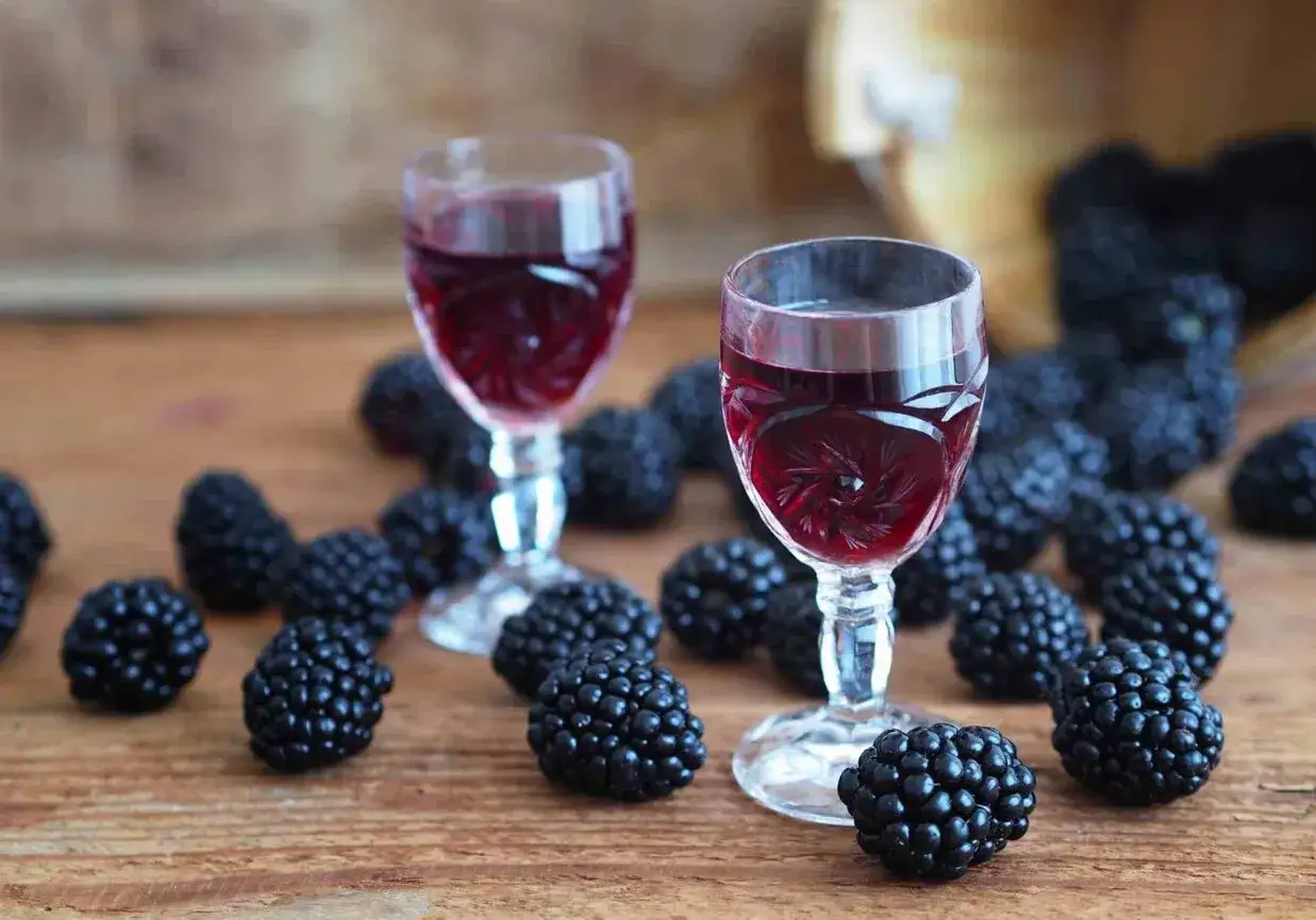Dwa kieliszki z rubinową nalewką z jerzyn, otoczone świeżymi owocami na drewnianym blacie.
