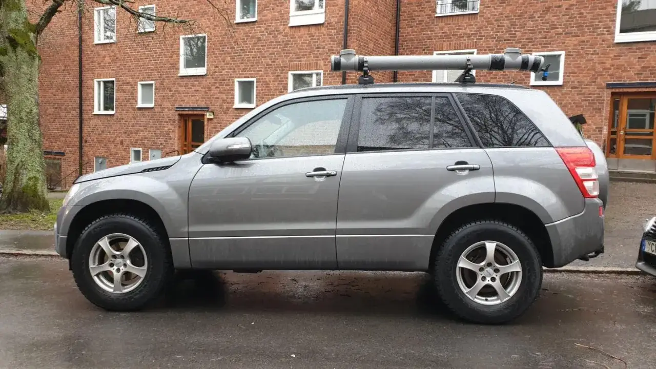 Gr&aring; Suzuki Grand Vitara med ett r&ouml;r p&aring; taket, kanske ett problem med transporten.