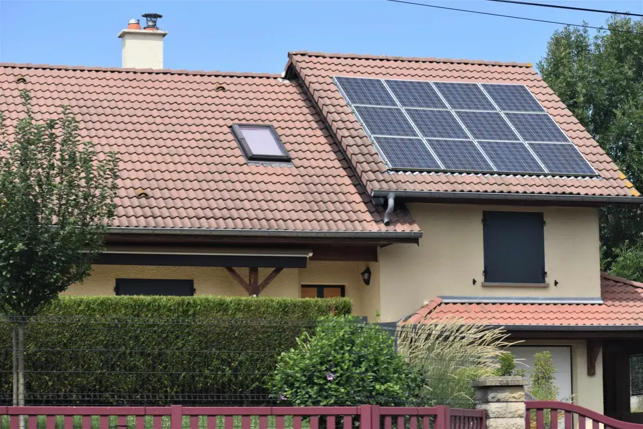 Mi experiencia con placas solares: tejado de casa con paneles solares, chimenea, ventana de tejado y setos.