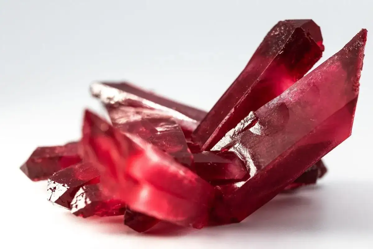 Cristalli rossi brillanti, simili a gemme, che ricordano il minerale del rubino, su sfondo bianco.