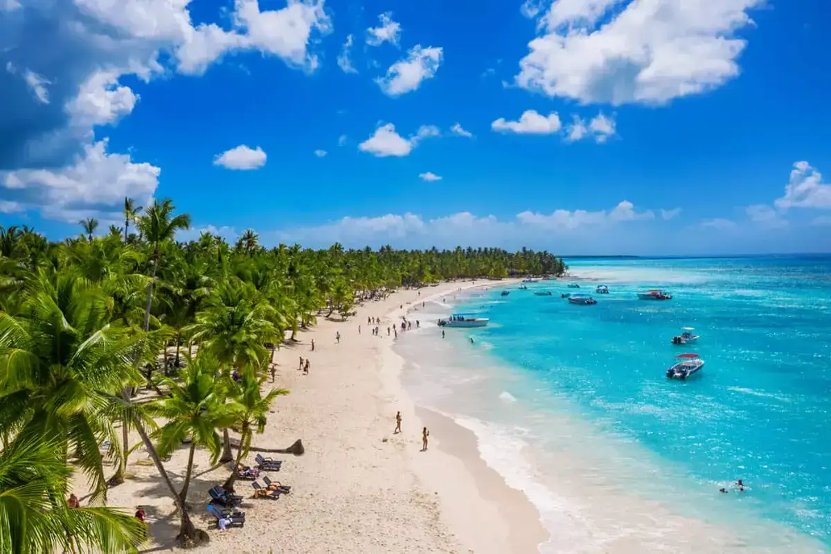 Traumhafter Strand mit Palmen und t&uuml;rkisfarbenem Wasser in der Dominikanischen Republik, Punta Cana. Boote schaukeln sanft auf dem Meer.