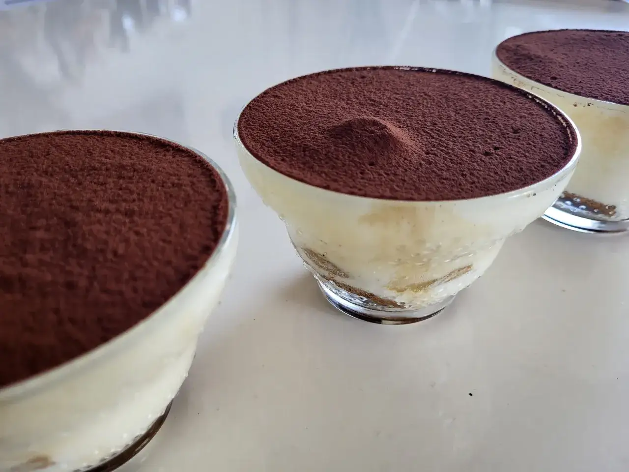 Trois verrines de tiramisu, pr&ecirc;tes &agrave; &ecirc;tre d&eacute;gust&eacute;es. Une recette simple et d&eacute;licieuse pour un dessert parfait.