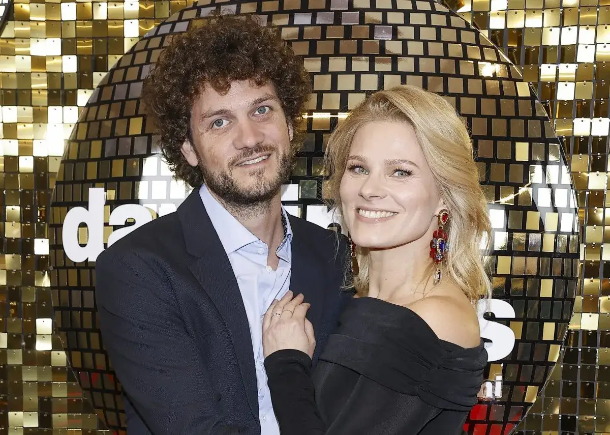 Anna Głogowska z partnerem pozują na tle błyszczącej ściany.